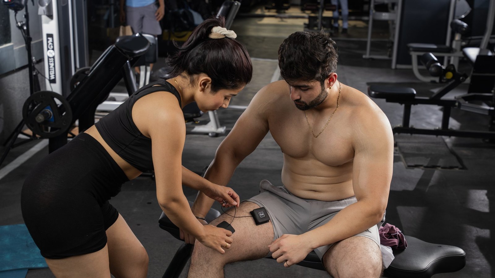 A trainer fitting a pod and spot pads to a man's thigh in the gym